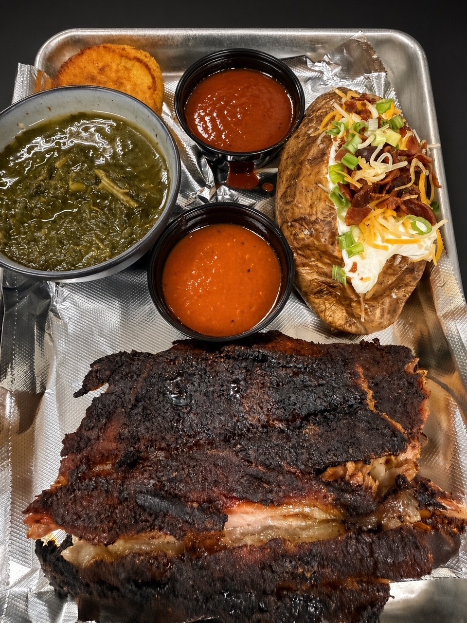Smoked ribs plate with collard greens, loaded baked potato & house sauces